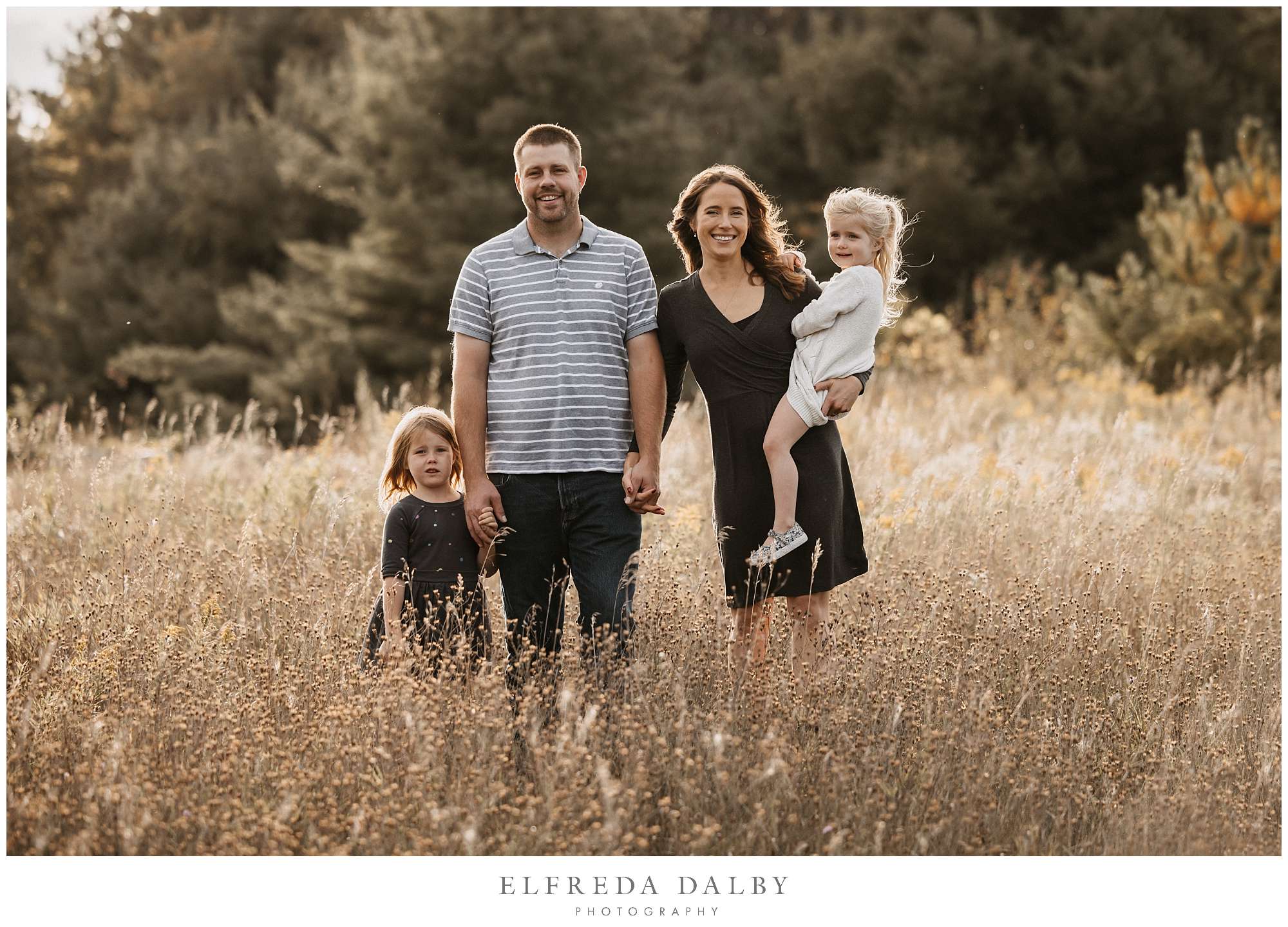 Mom and dad with their two little girls standing in a field during golden hour